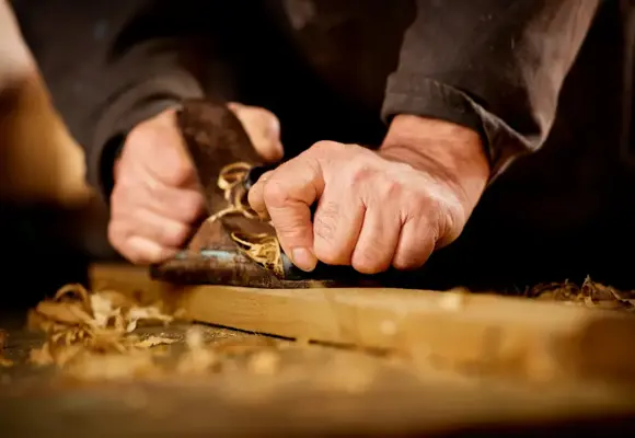 Man using a planar to smooth the surface of wood