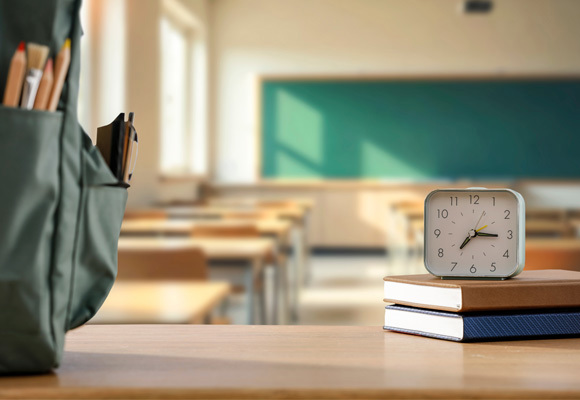 Clock above a stack of books with classroom background